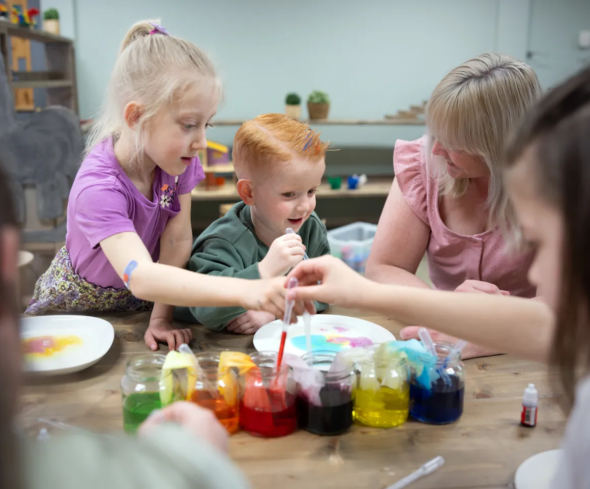 kinderen worden door een pedagogisch medewerker begeleid met het verven bij kinderopvang Kind&co ludens