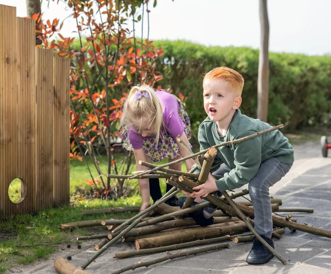 Kinderen spelen met takken buiten bij kinderopvang Kind&co ludens