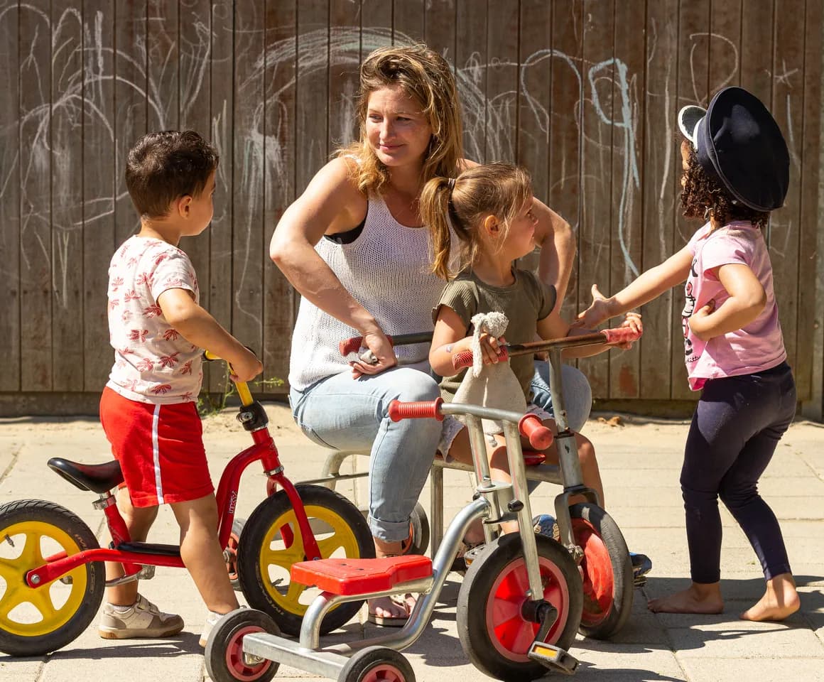 Kinderen van de peutergroep spelen samen met de pedagogisch medewerker buiten met de fiets bij kinderopvang Kind&co ludens