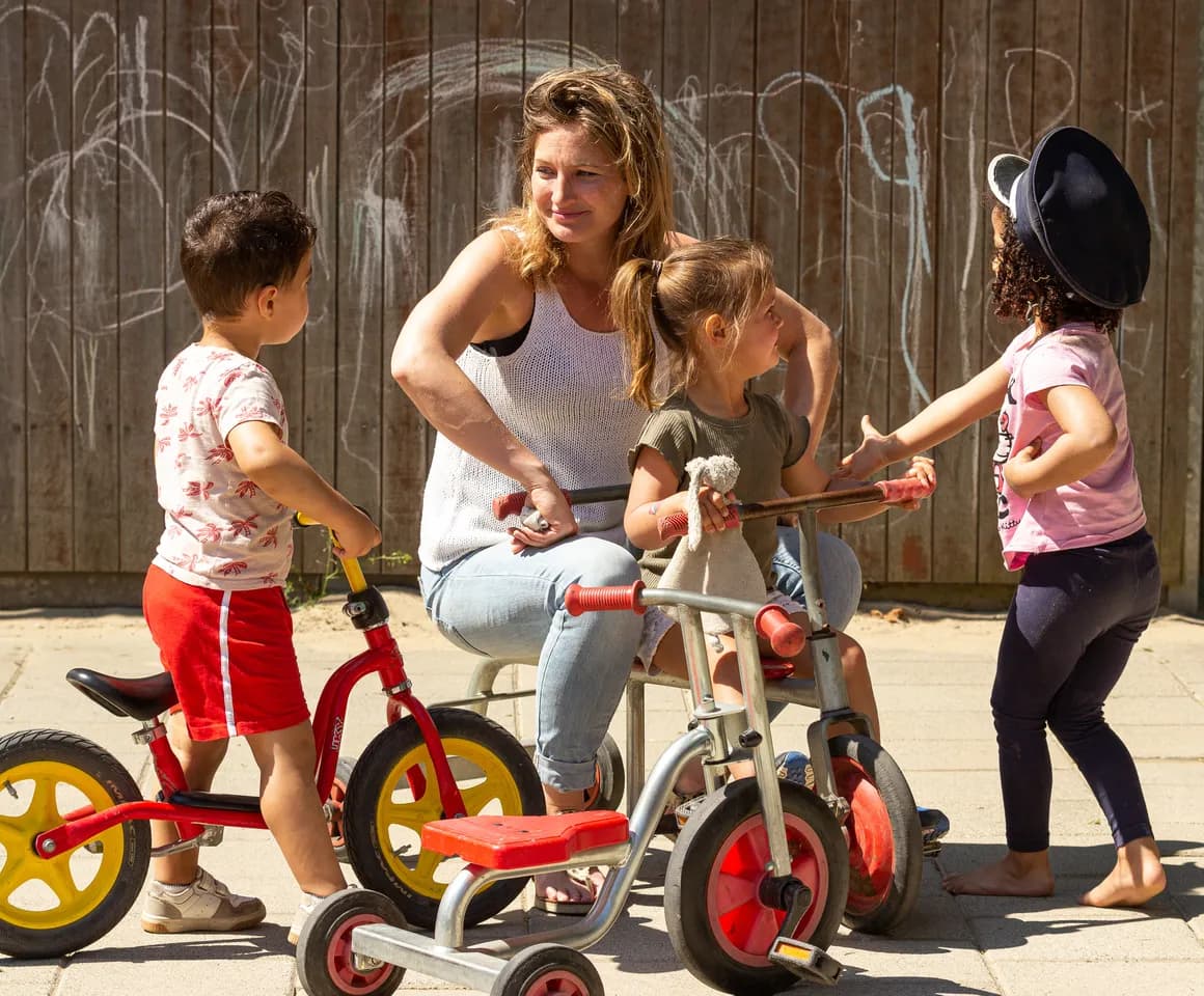Kinderen van de peutergroep spelen samen met de pedagogisch medewerker buiten met de fiets bij kinderopvang Kind&co ludens