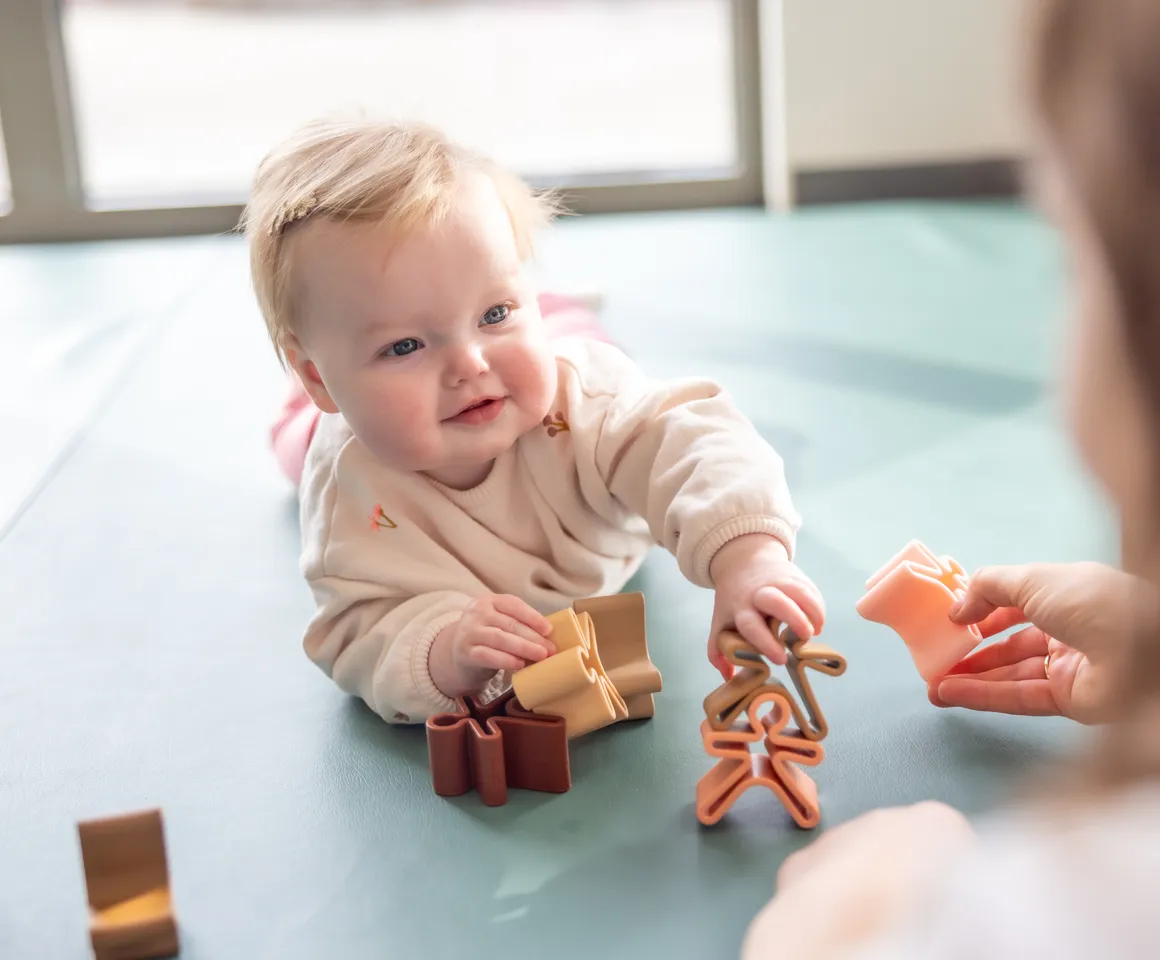 Baby speelt met houten speelgoed poppetjes bij gastouder van kinderopvang Kind&co ludens