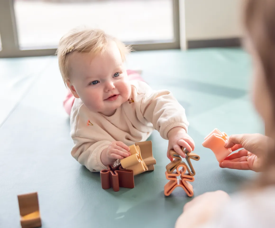 Baby speelt met houten speelgoed poppetjes bij gastouder van kinderopvang Kind&co ludens