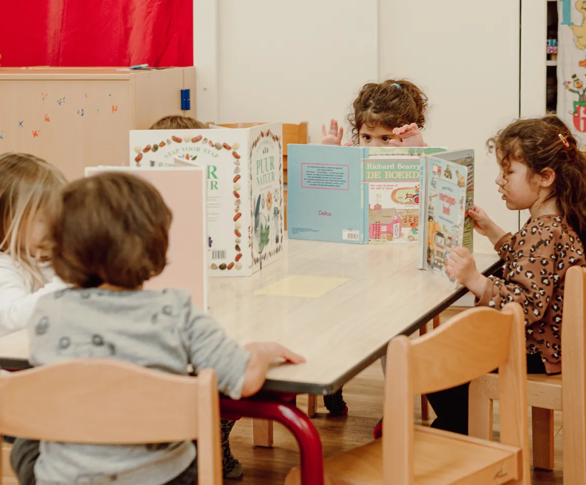 Kinderen van de peutergroep lezen samen aan tafel bij kinderopvang Kind&co ludens