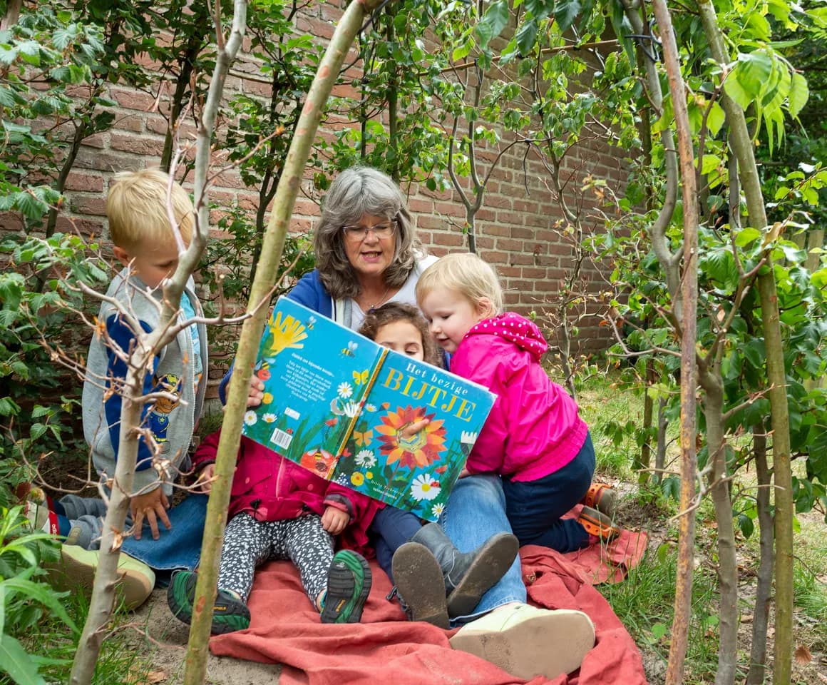 Pedagogisch medewerker leest kinderen in de tuin voor bij kinderdagverblijf 't Elfenbankje, kinderopvang Kind&co ludens