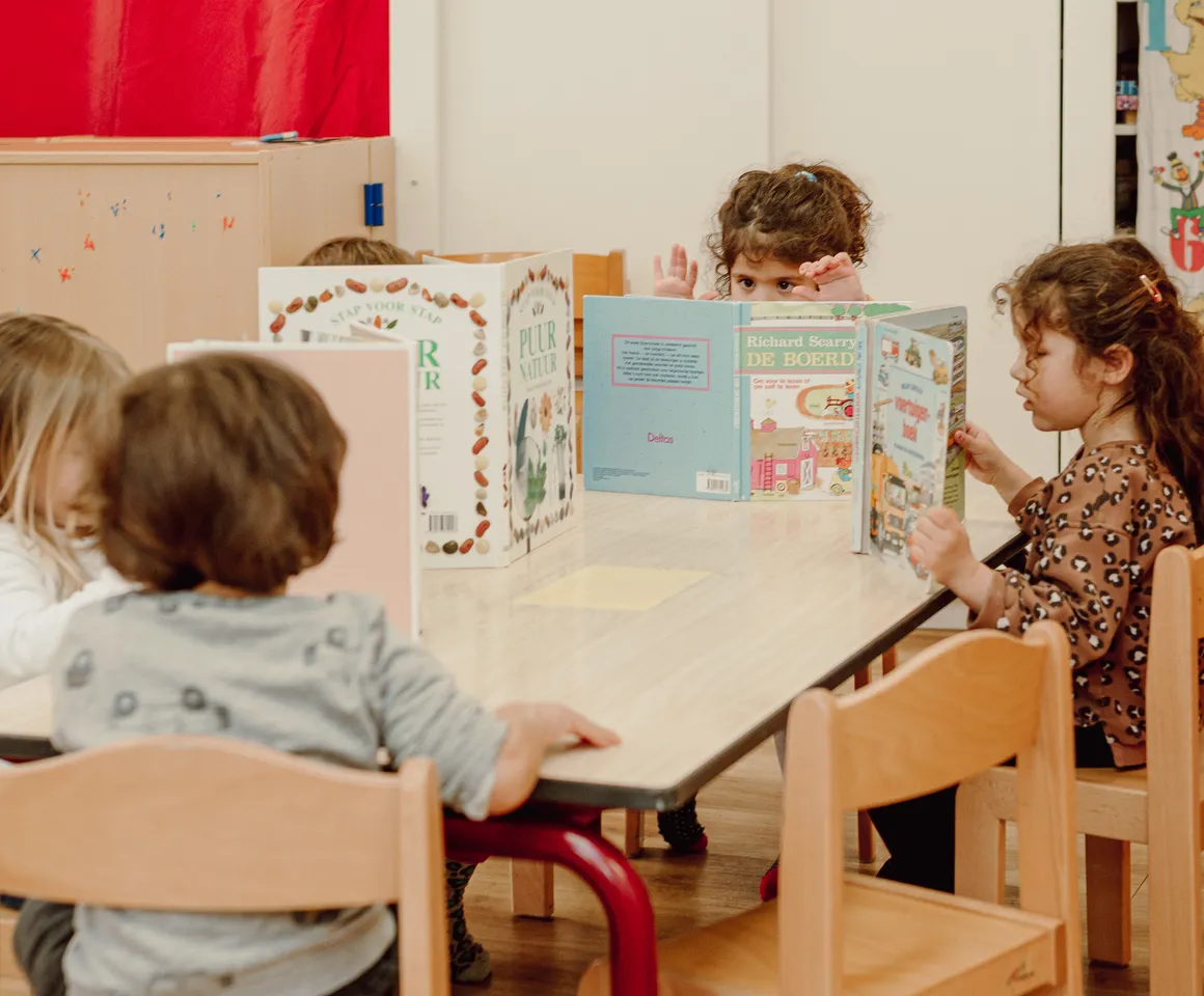 Kinderen van de peutergroep lezen samen aan tafel bij kinderopvang Kind&co ludens