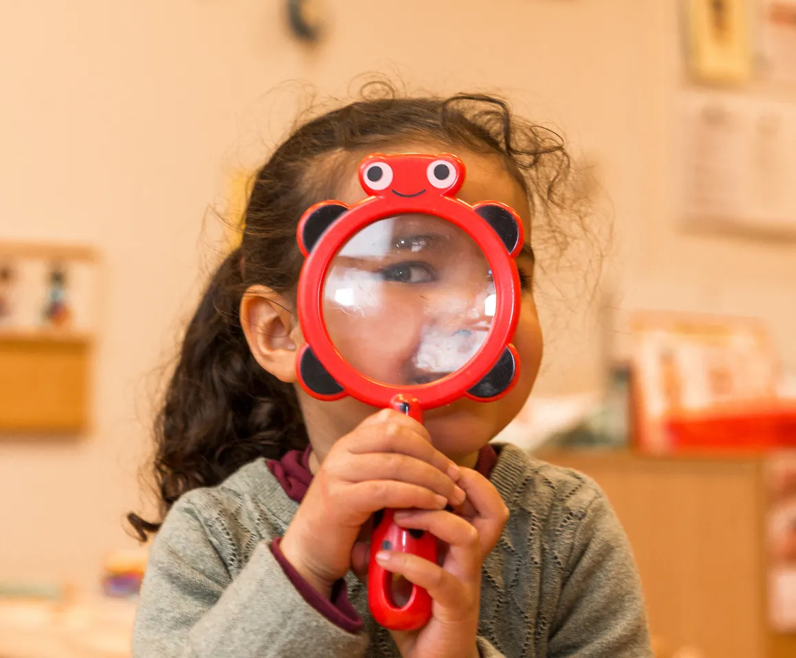 Kind op de peutergroep speelt met vergrootglas bij kinderopvang Kind&co ludens