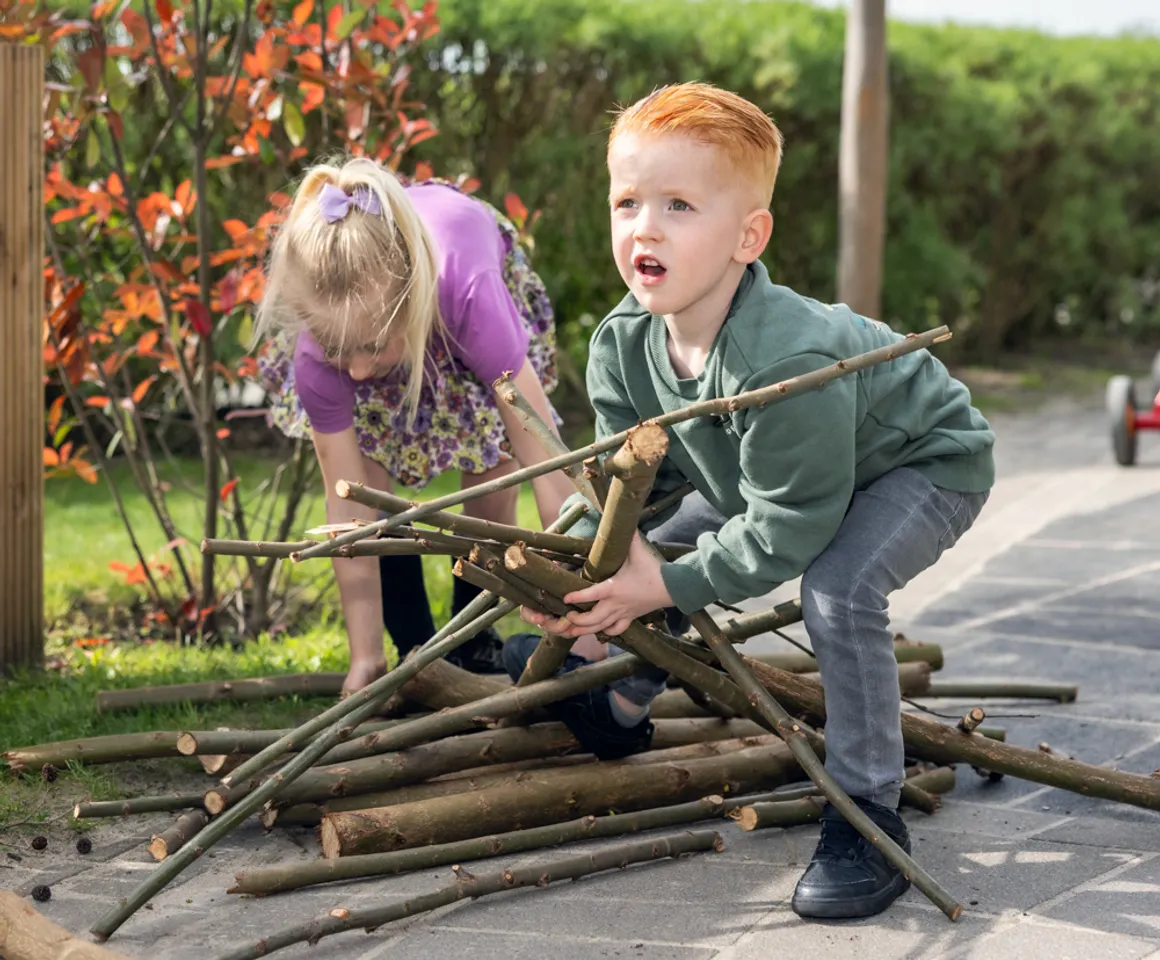 Kinderen spelen met takken buiten bij kinderopvang Kind&co ludens