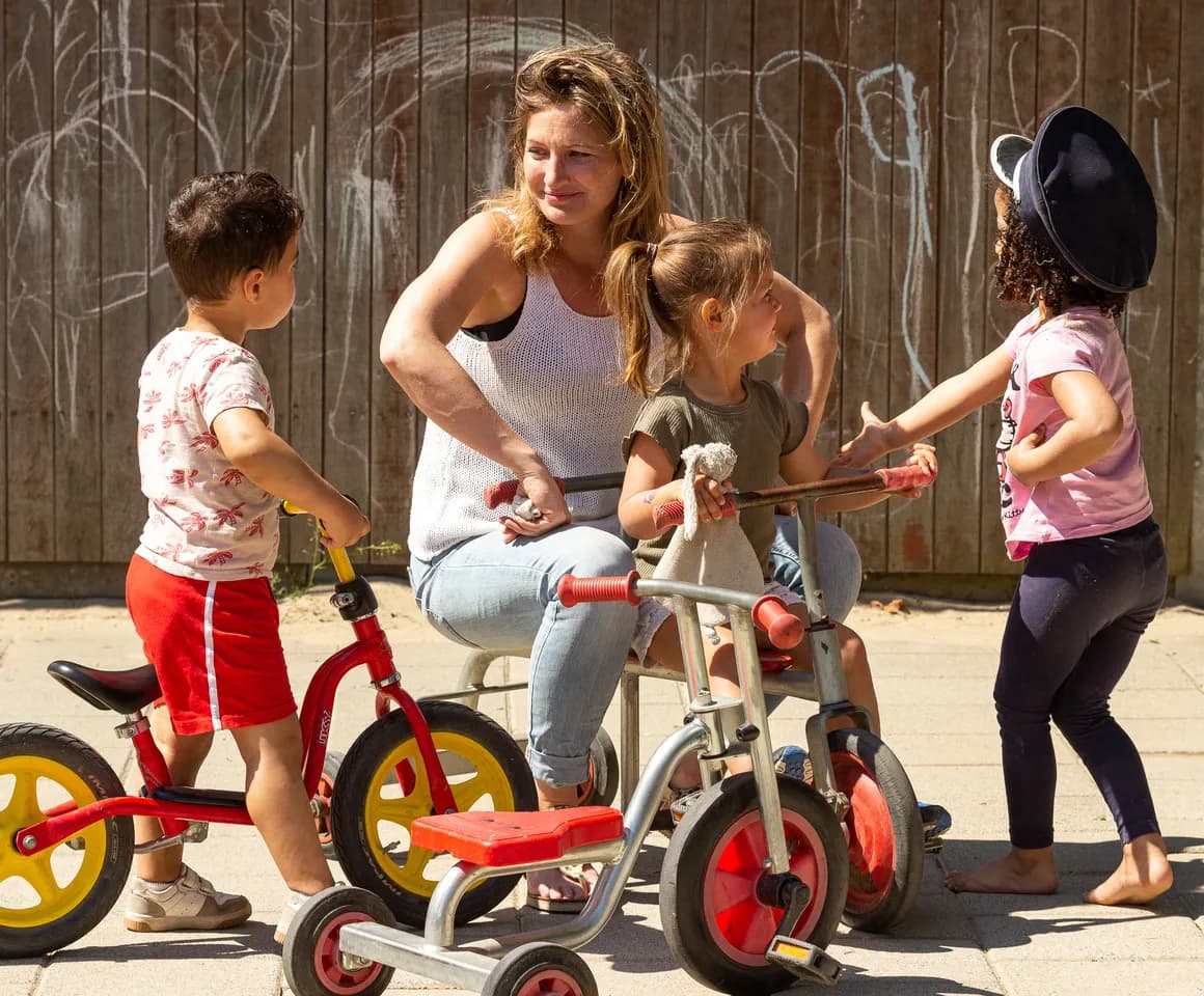 Kinderen van de peutergroep spelen samen met de pedagogisch medewerker buiten met de fiets bij kinderopvang Kind&co ludens