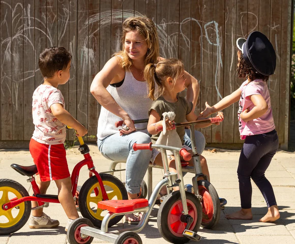 Kinderen van de peutergroep spelen samen met de pedagogisch medewerker buiten met de fiets bij kinderopvang Kind&co ludens