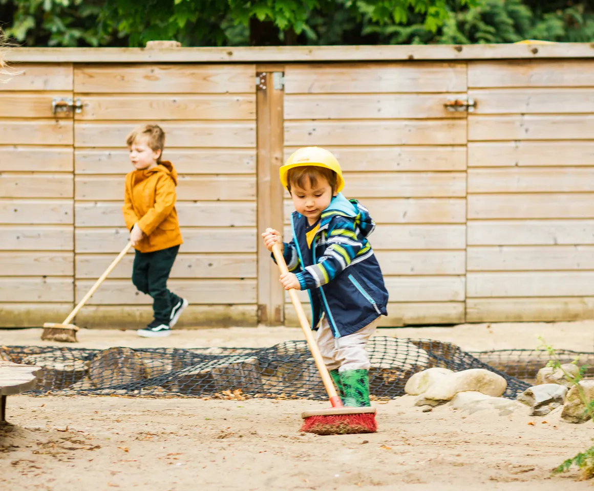 Kinderen samen met de pedagogisch medewerker buiten aan het vegen bij kinderopvang Kind&co ludens