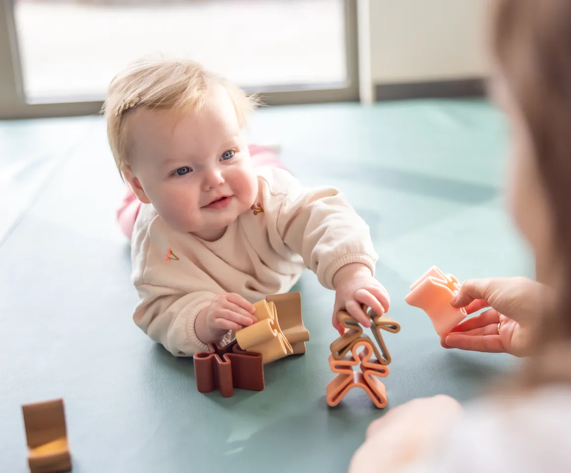 Baby speelt met  houten speelgoed poppetjes bij gastouder van kinderopvang Kind&co ludens