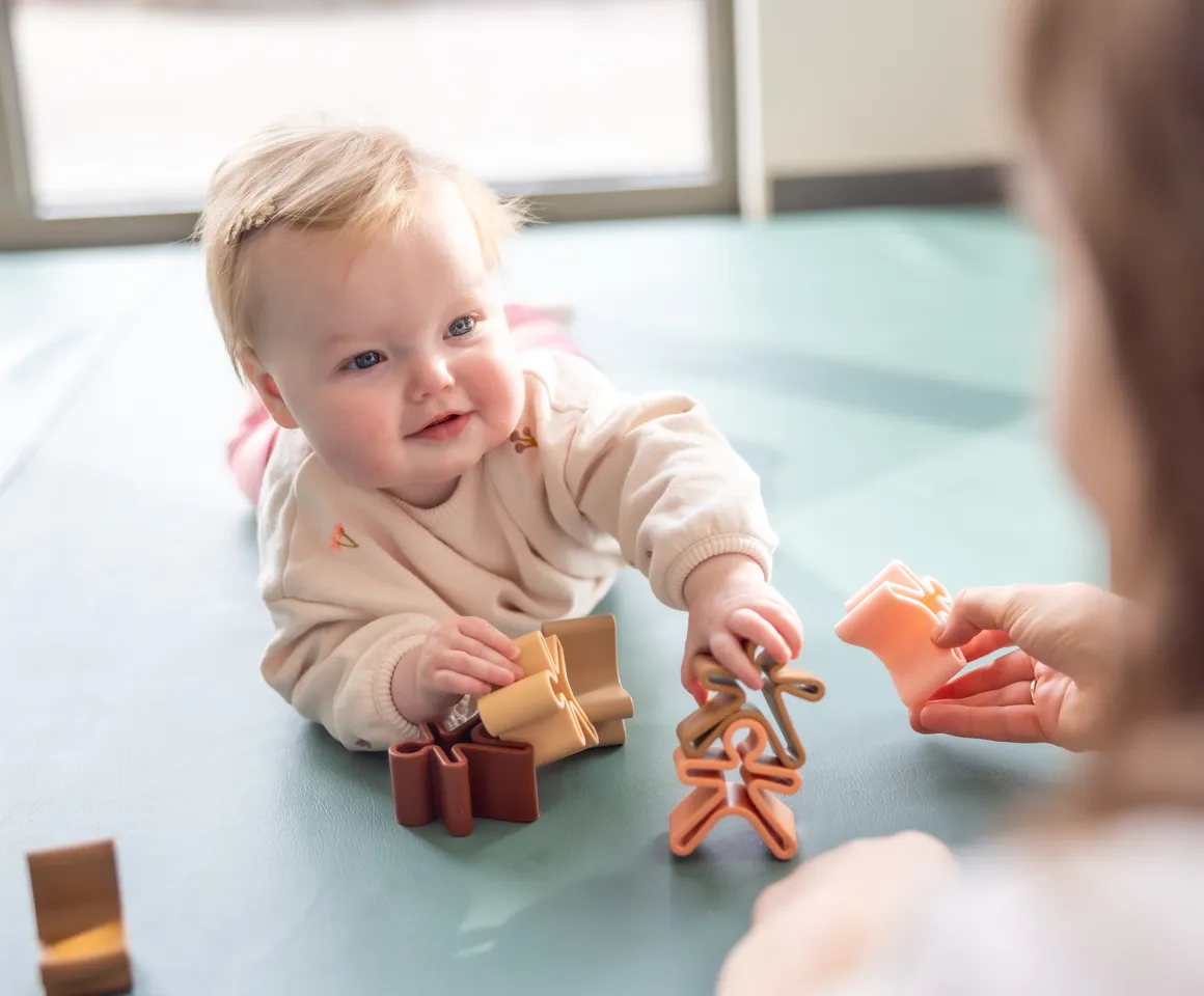 Baby speelt met houten speelgoed poppetjes bij gastouder van kinderopvang Kind&co ludens