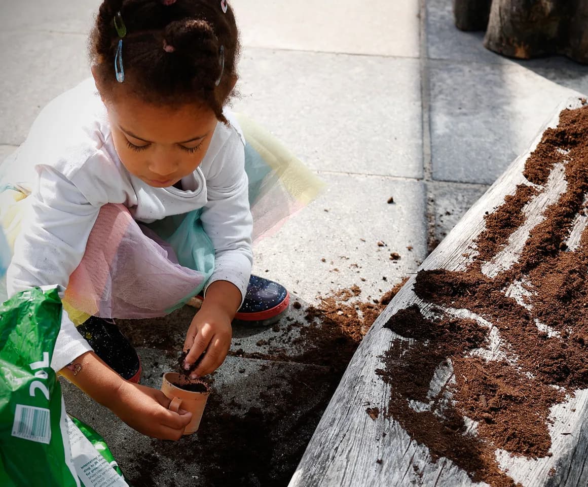 Kind van de peutergroep poot zaadjes in de moestuin bij kinderopvang Kind&co ludens