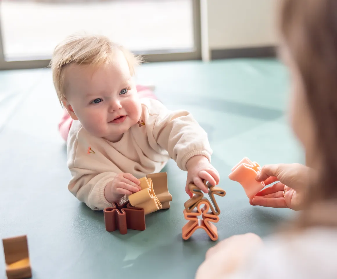 Baby speelt met houten speelgoed poppetjes bij gastouder van kinderopvang Kind&co ludens
