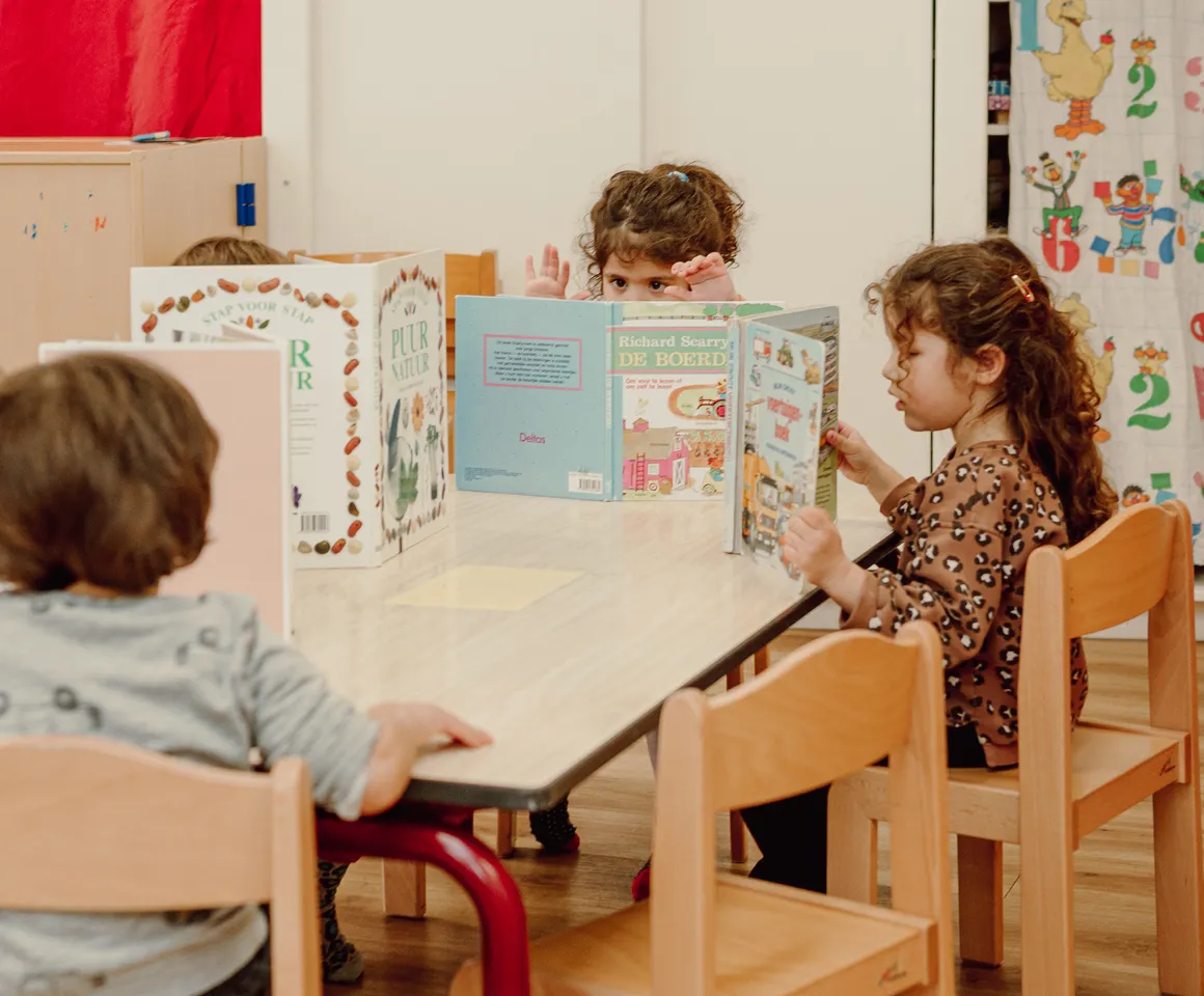 Kinderen van de peutergroep lezen samen aan tafel bij kinderopvang Kind&co ludens