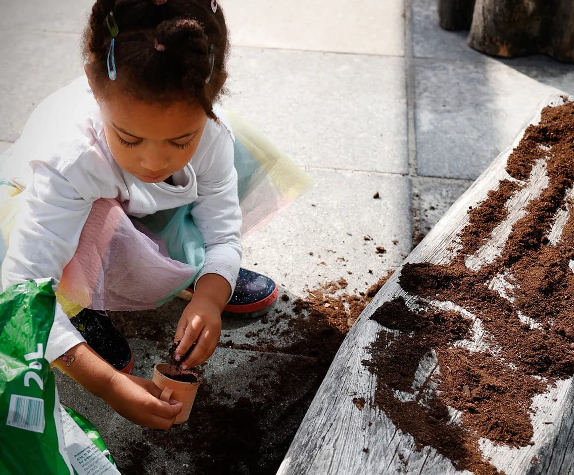 Kind van de peutergroep poot zaadjes in de moestuin bij kinderopvang Kind&co ludens