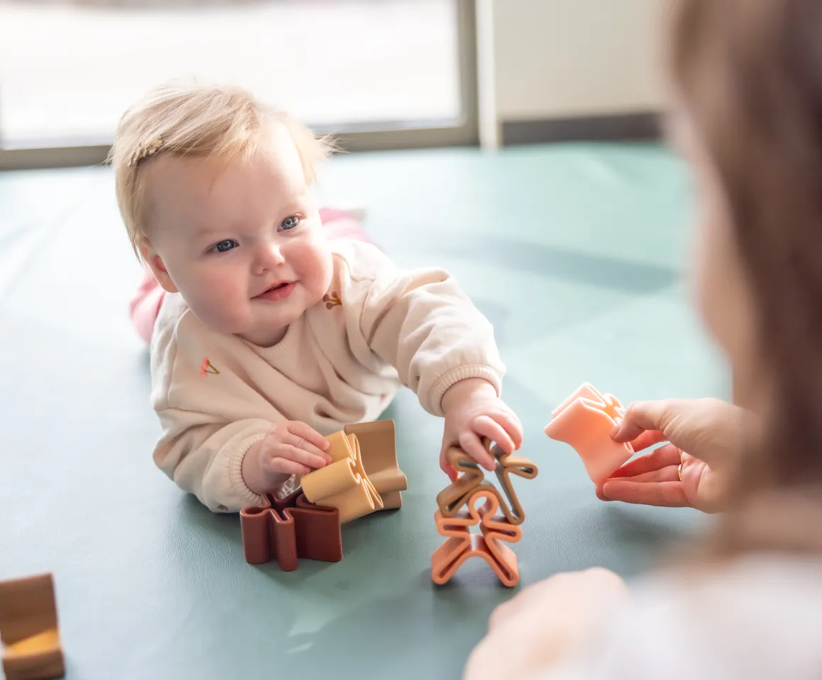 Baby speelt met houten speelgoed poppetjes bij gastouder van kinderopvang Kind&co ludens