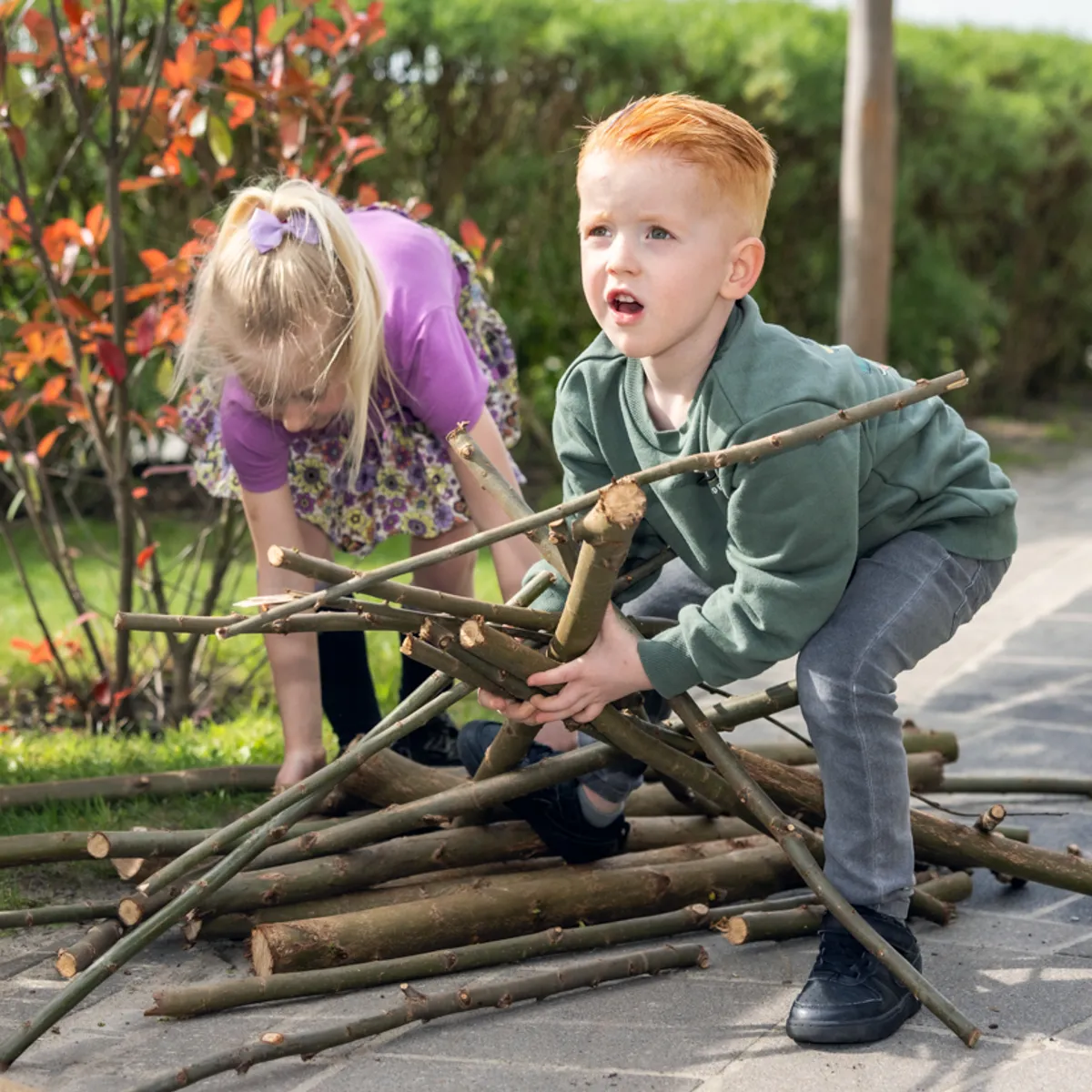 Kinderen spelen met takken buiten bij kinderopvang Kind&co ludens