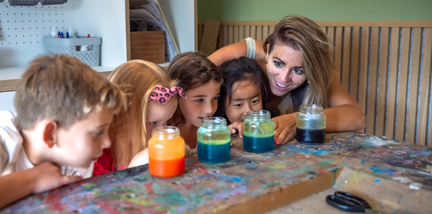 Kinderen kijken met pedagogisch medewerker naar pot met gekleurd water bij kinderopvang Kind&co ludens