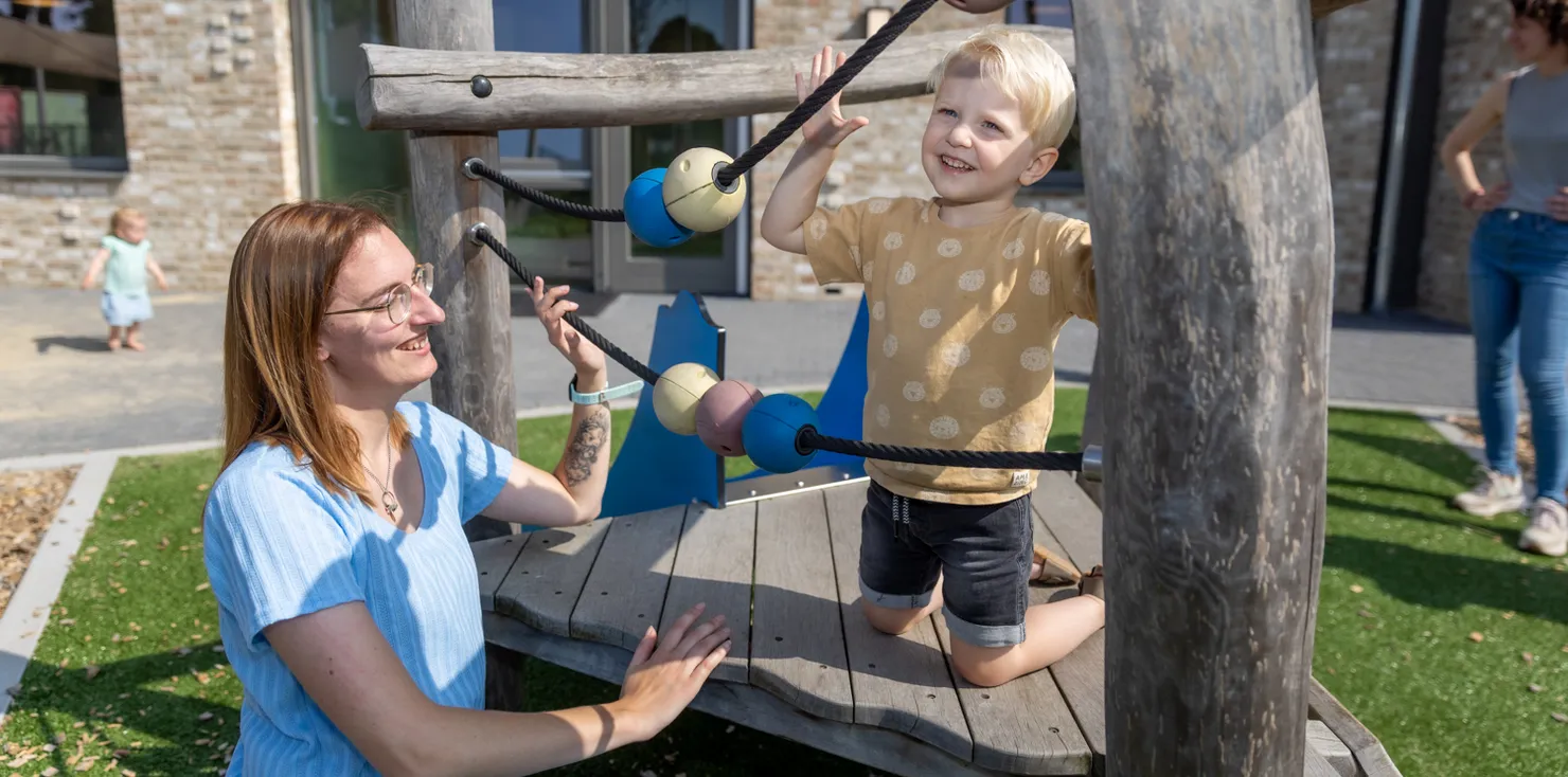 Kind klimt buiten met pedagogisch medewerker bij kinderopvang Kind&co ludens