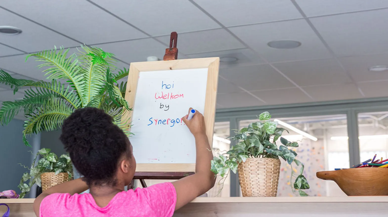 Kind schrijft welkomst tekst op bord bij buitenschoolse opvang Synergo, Kind&co ludens