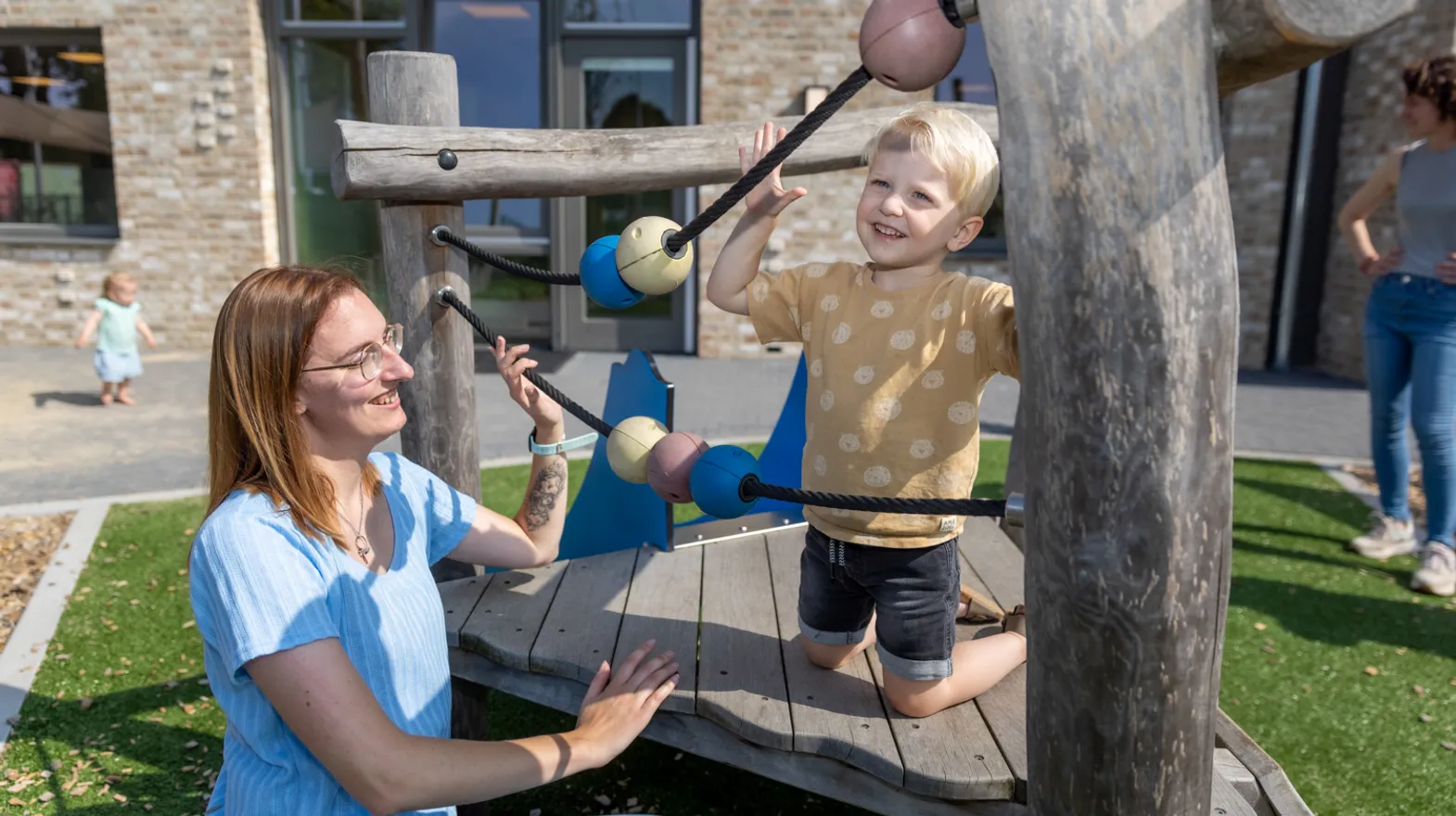 Kind klimt buiten met pedagogisch medewerker bij kinderopvang Kind&co ludens
