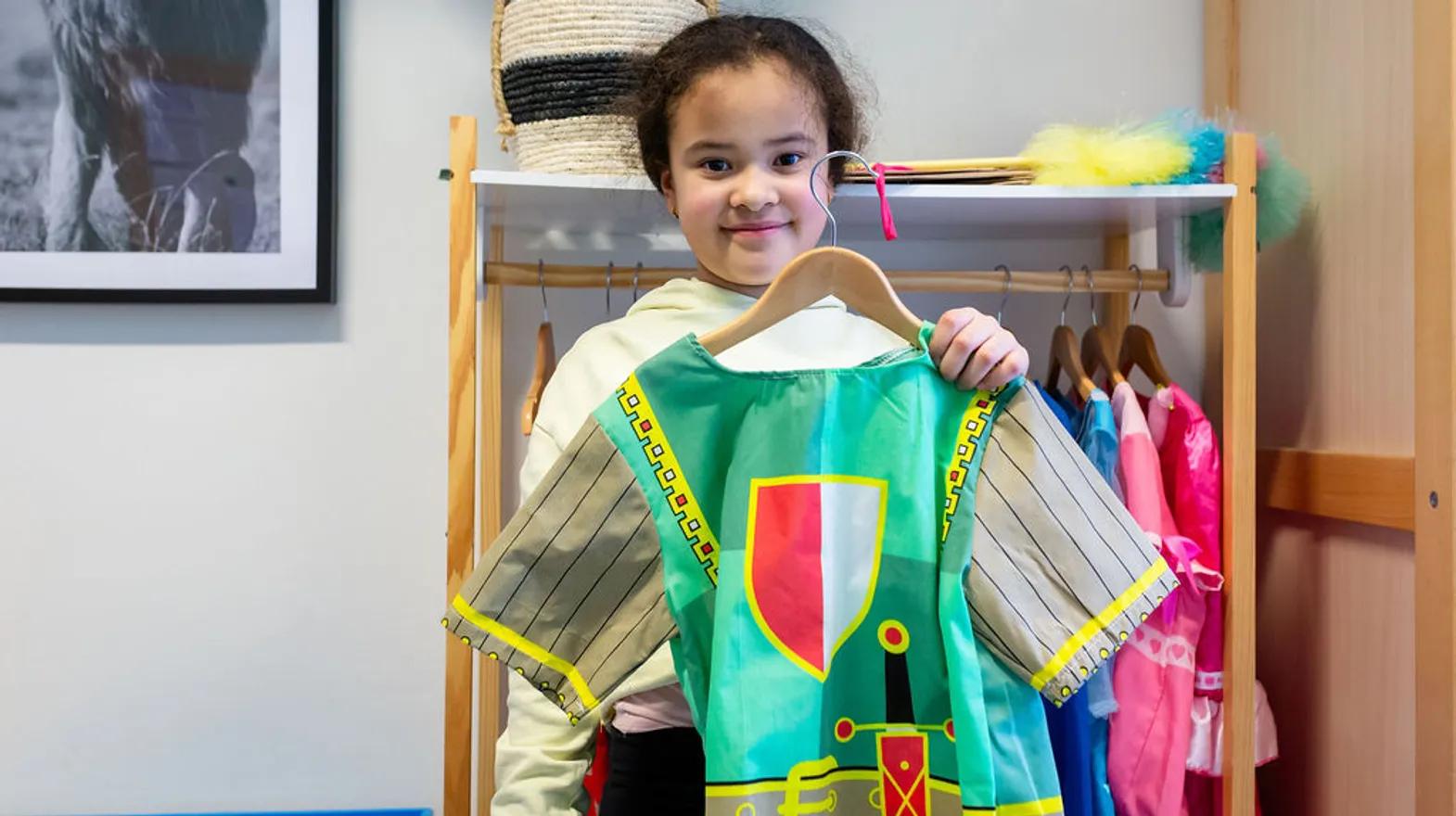 Kind staat bij de verkleedkleren en laat een ridderpak zien bij buitenschoolse opvang Villa Bekema, kinderopvang Kind&co Ludens