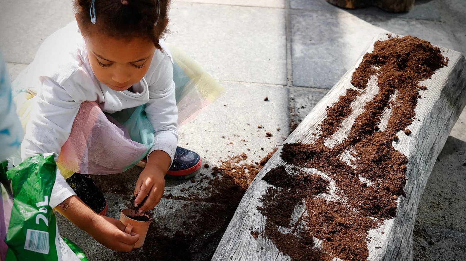 Kind van de peutergroep poot zaadjes in de moestuin bij kinderopvang Kind&co ludens