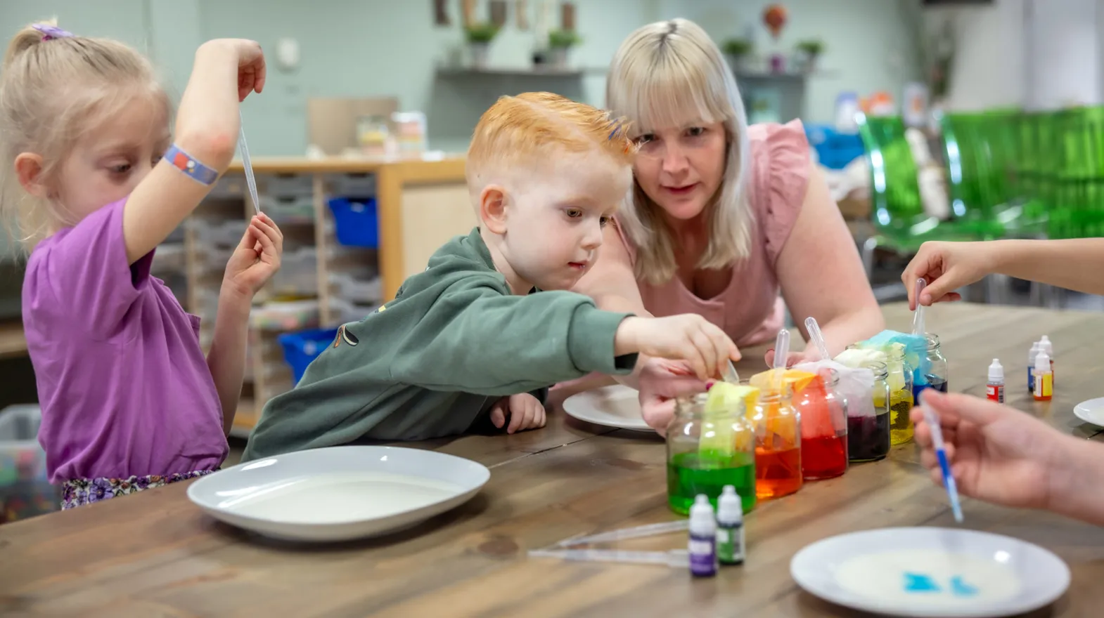 kinderen worden door een pedagogisch medewerker begeleid met het verven bij kinderopvang Kind&co ludens