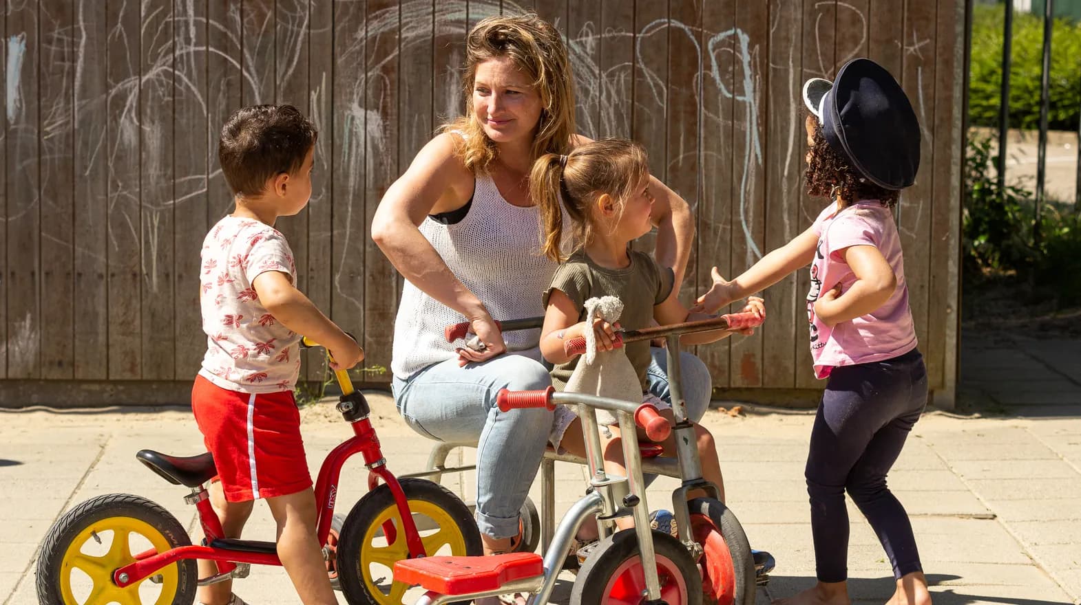Kinderen van de peutergroep spelen samen met de pedagogisch medewerker buiten met de fiets bij kinderopvang Kind&co ludens