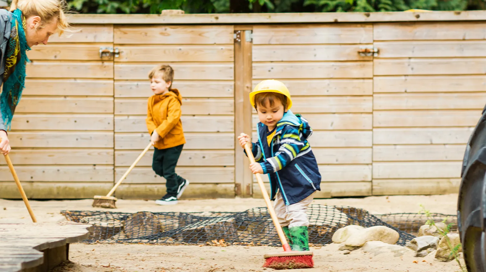 Kinderen samen met de pedagogisch medewerker buiten aan het vegen bij kinderopvang Kind&co ludens