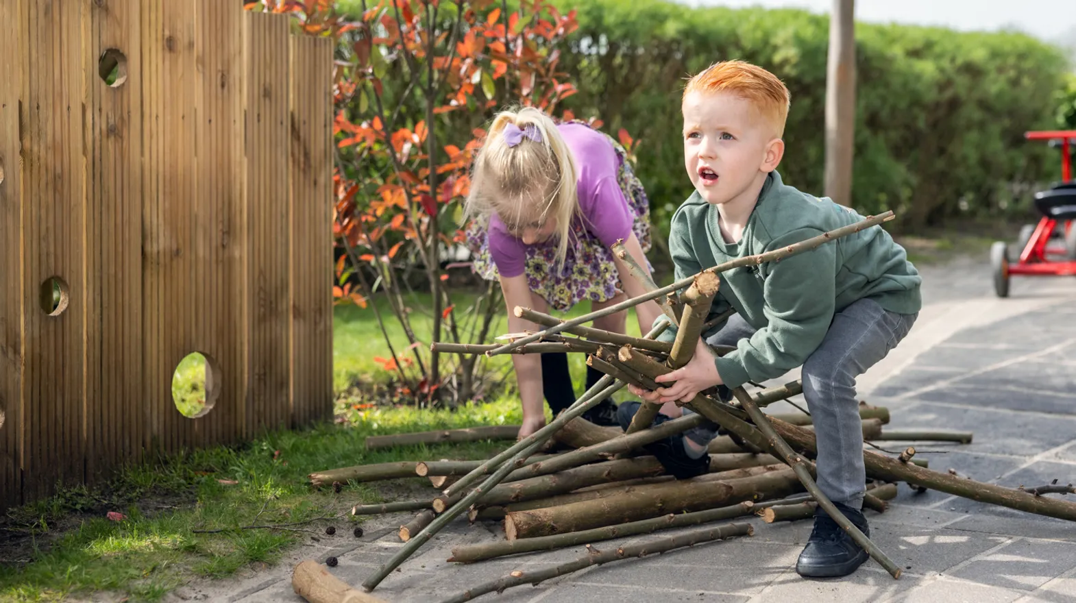 Kinderen spelen met takken buiten bij kinderopvang Kind&co ludens