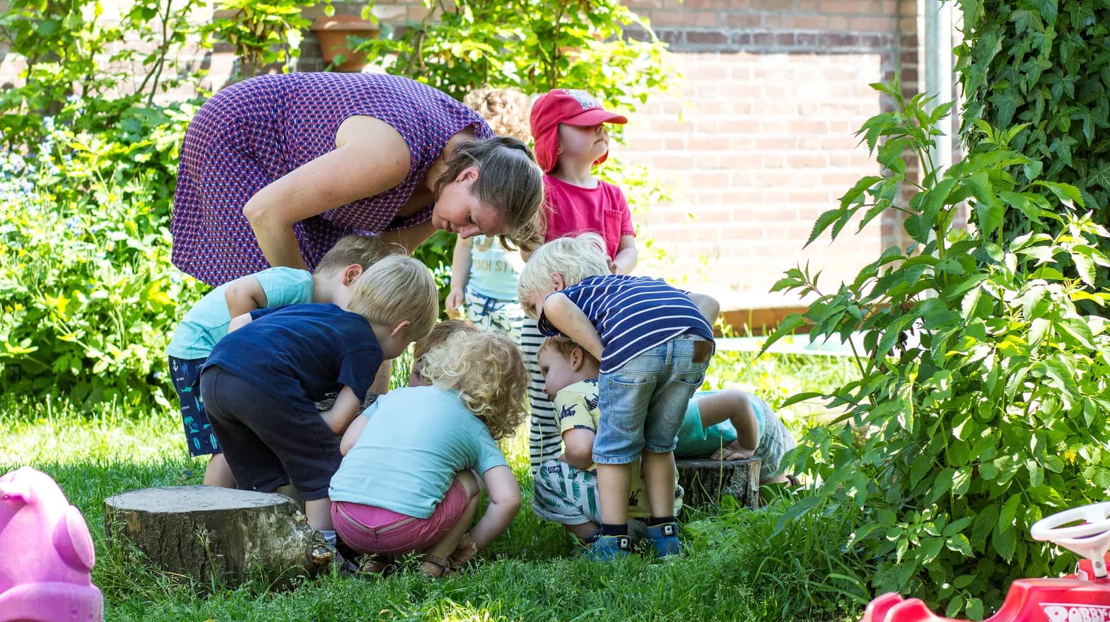 Kinderen kijken met elkaar in een kring naar iets wat in de tuin ligt bij kinderdagverblijf Jodokus, kinderopvang Kind&co ludens