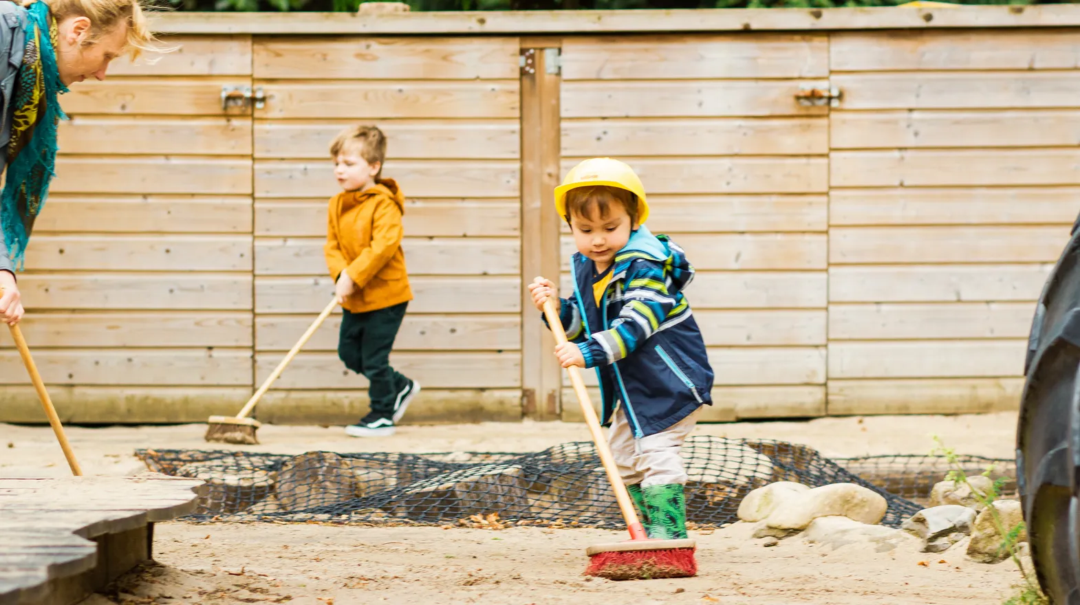 Kinderen samen met de pedagogisch medewerker buiten aan het vegen bij kinderopvang Kind&co ludens