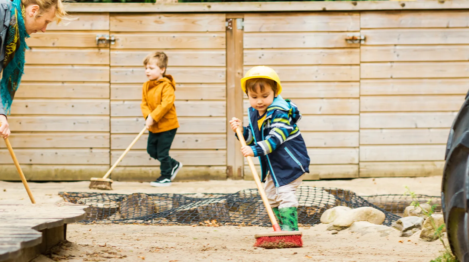 Kinderen samen met de pedagogisch medewerker buiten aan het vegen bij kinderopvang Kind&co ludens