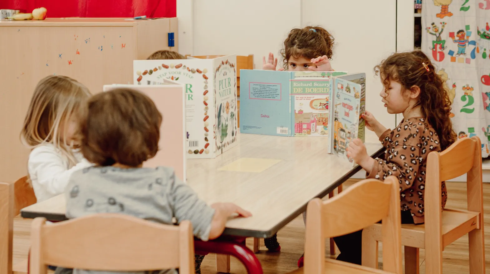 Kinderen van de peutergroep lezen samen aan tafel bij kinderopvang Kind&co ludens