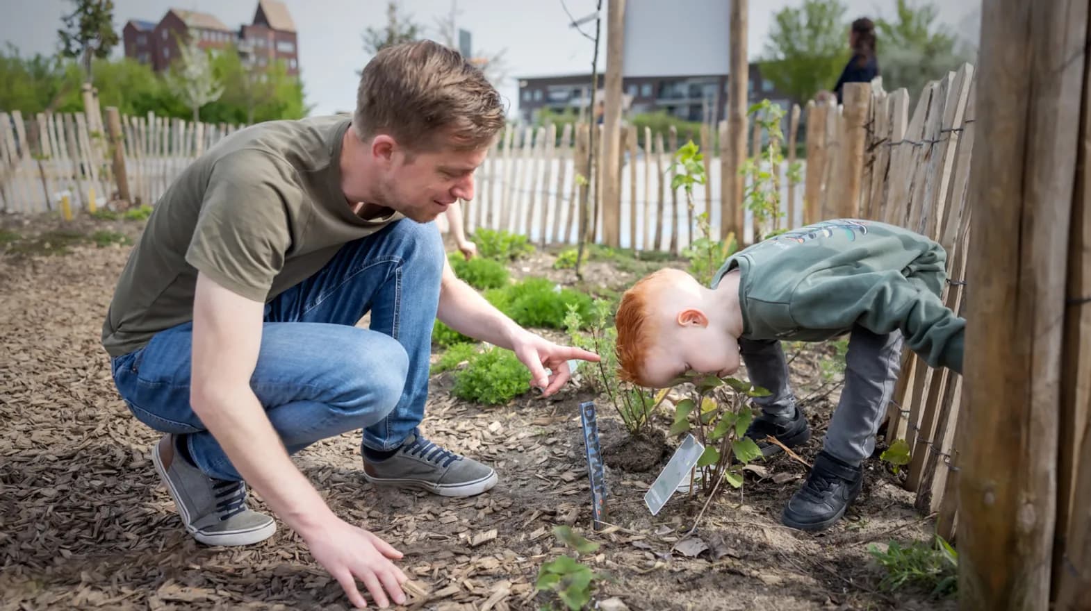 Kind ruikt aan bloem in tuin met pedagogisch medewerker bij kinderopvang Kind&co ludens