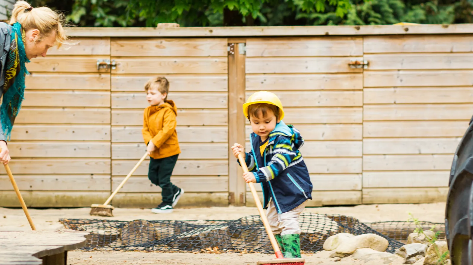Kinderen samen met de pedagogisch medewerker buiten aan het vegen bij kinderopvang Kind&co ludens