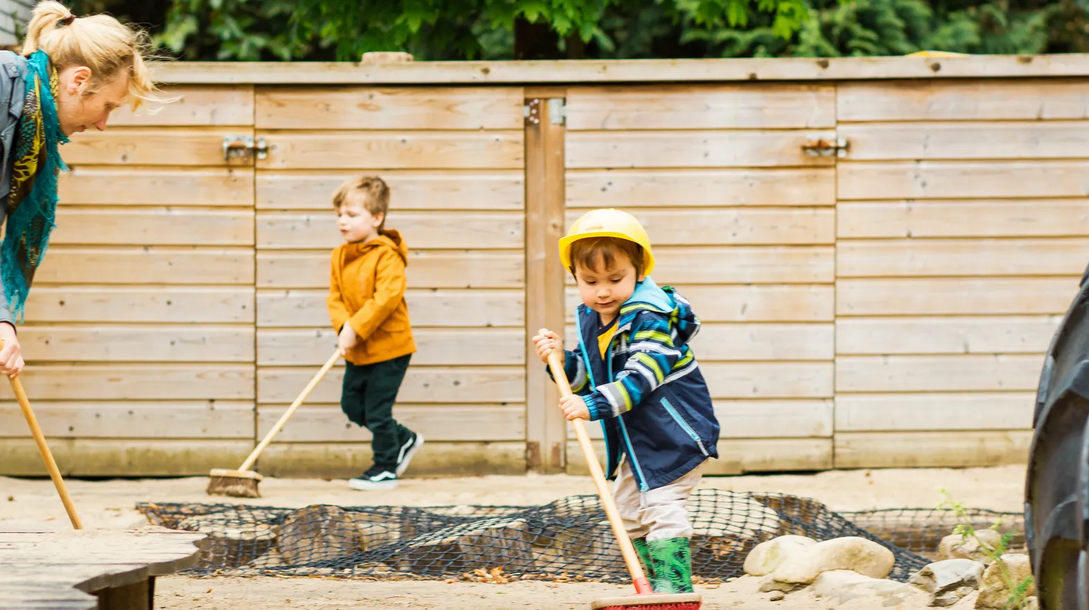 Kinderen samen met de pedagogisch medewerker buiten aan het vegen bij kinderopvang Kind&co ludens