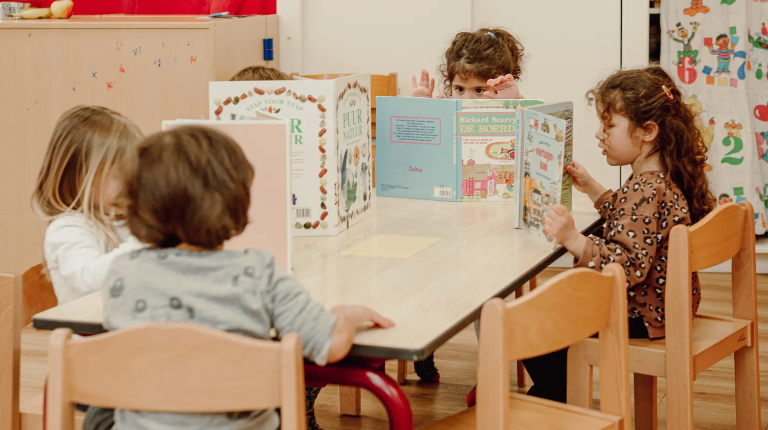 Kinderen van de peutergroep lezen samen aan tafel bij kinderopvang Kind&co ludens