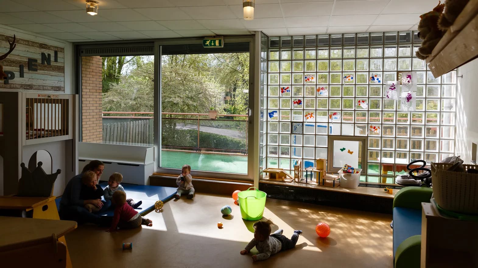 Pedagogisch medewerker speelt met de kinderen op de grond bij kinderdagverblijf Harlekijn, kinderopvang Kind&co ludens
