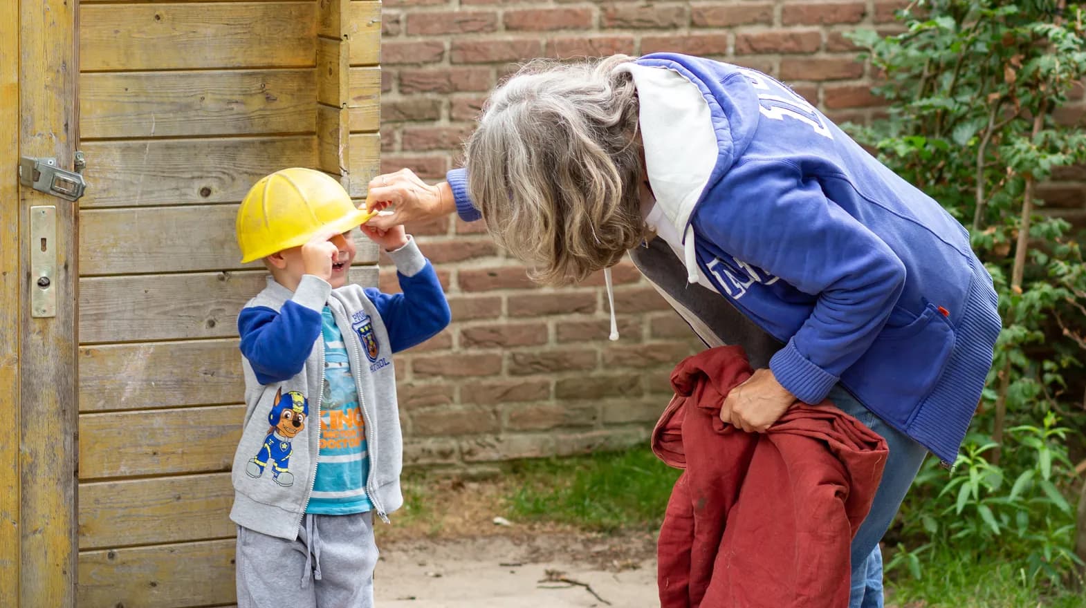 Kind speelt lachend met bouwhelm in de tuin van kinderdagverblijf 't Elfenbankje, kinderopvang Kind&co ludens