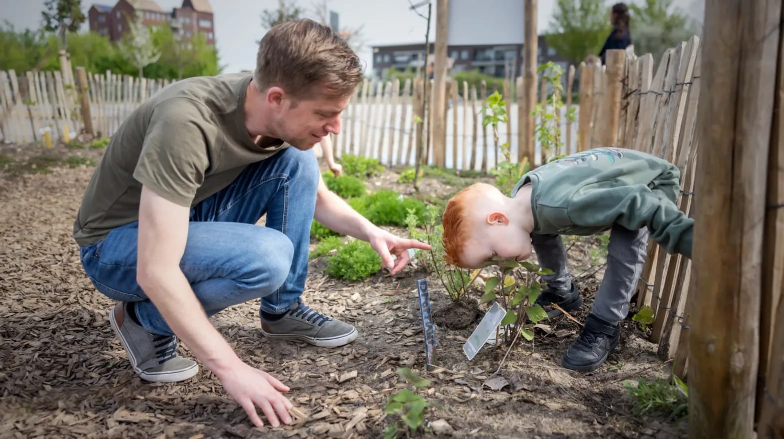 Kind ruikt aan bloem in tuin met pedagogisch medewerker bij kinderopvang Kind&co ludens