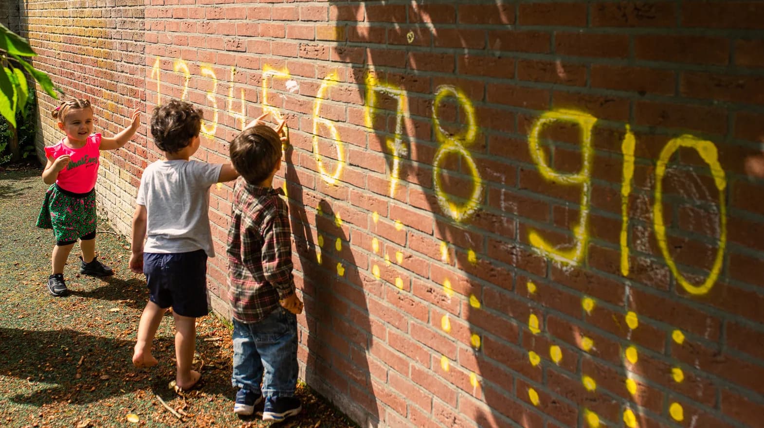 Kinderen staan buiten bij een muur waar cijfers op staan bij peuteropvang 't Egeltje, Kind&co ludens