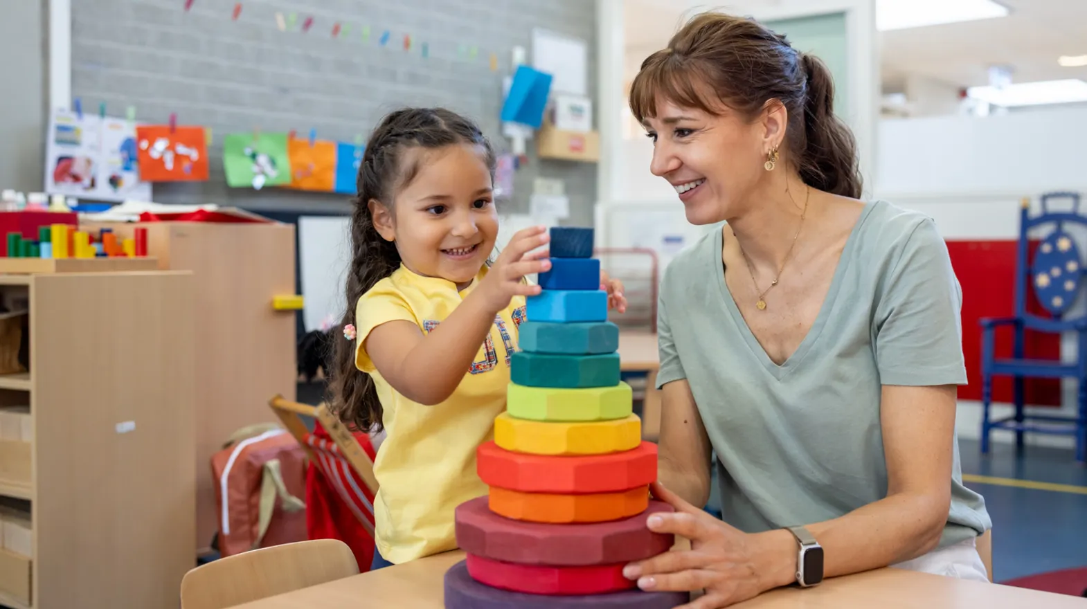 Kind stapelt houten ringen samen met pedagogisch medewerker bij kinderopvang Kind&co ludens