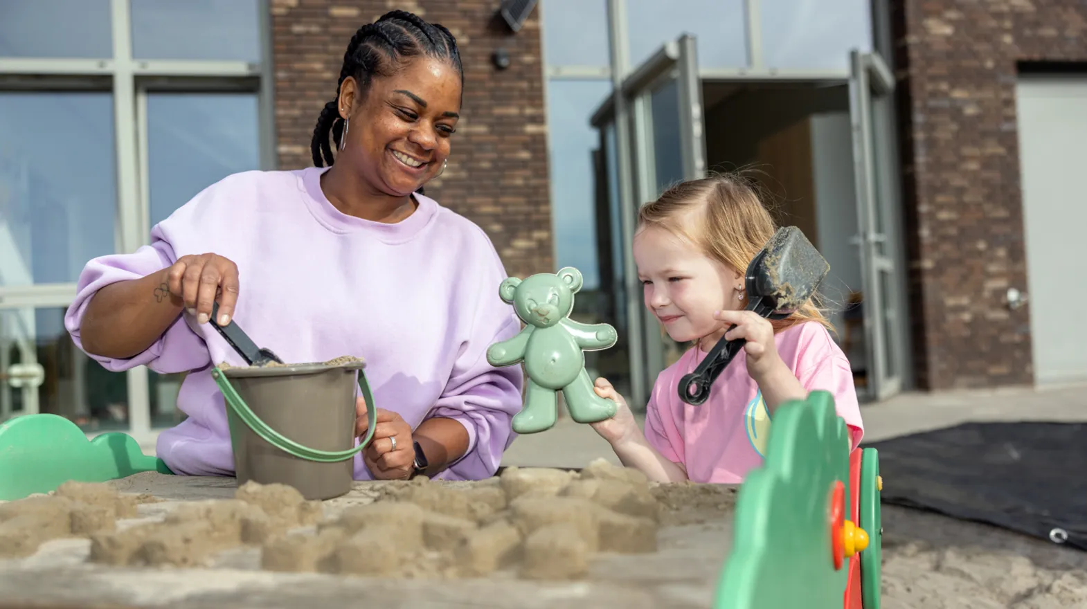 Kind maakt zandtaart in zandbak met pedagogisch medewerker bij Kind&co ludens