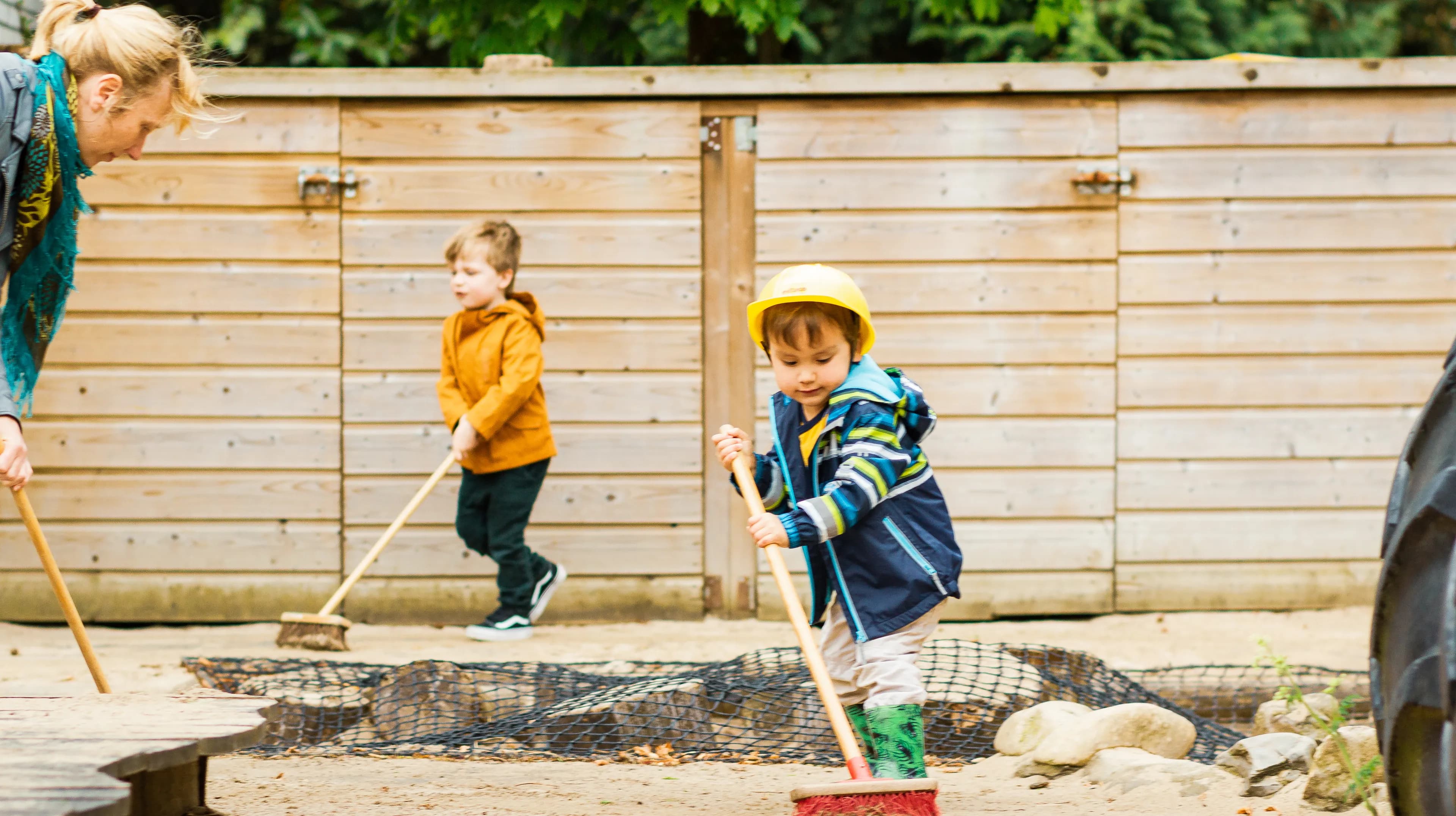 Kinderen samen met de pedagogisch medewerker buiten aan het vegen bij kinderopvang Kind&co ludens