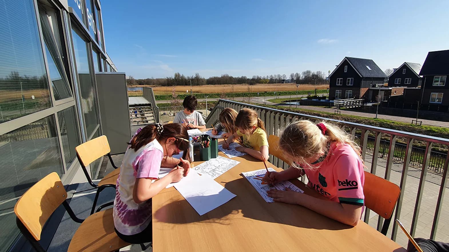 Kinderen schrijvend aan tafel in de buitenruimte bij BSO-Kersenbende van kinderopvang Kind&co ludens
