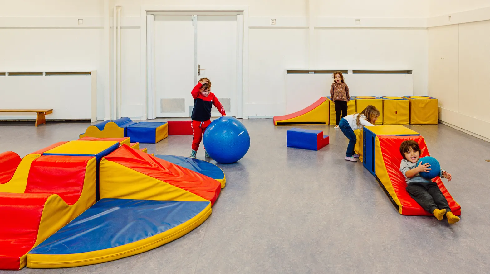 Kinderen klimmen en klauteren over speelkussens in de gymzaal bij peuteropvang Warmoes, kinderopvang Kind&co ludens