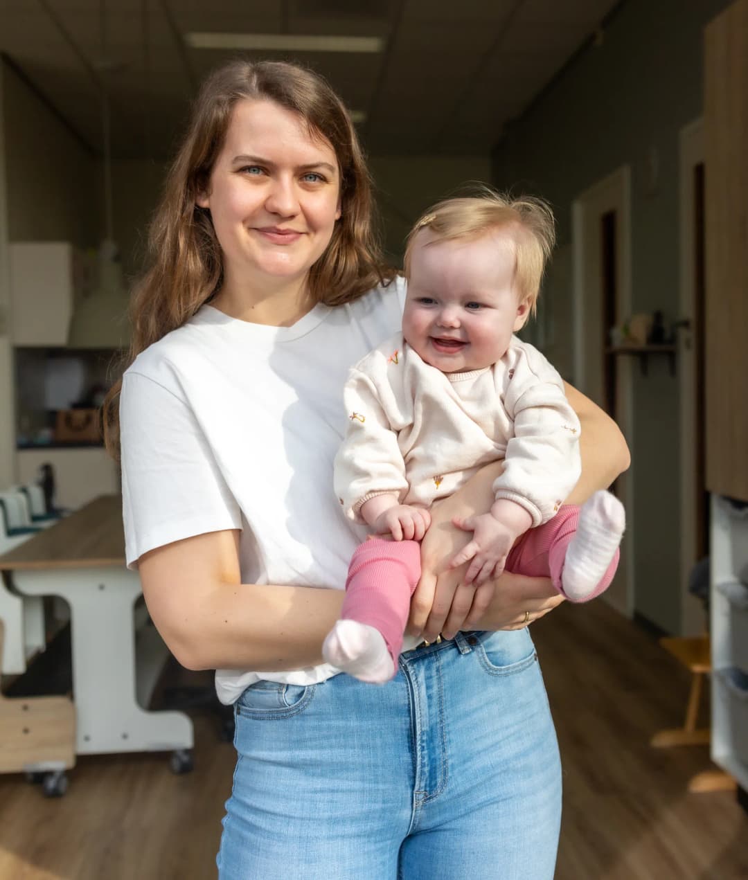 Blije baby in handen van een pedagogisch medewerker bij kinderopvang Kind&co ludens
